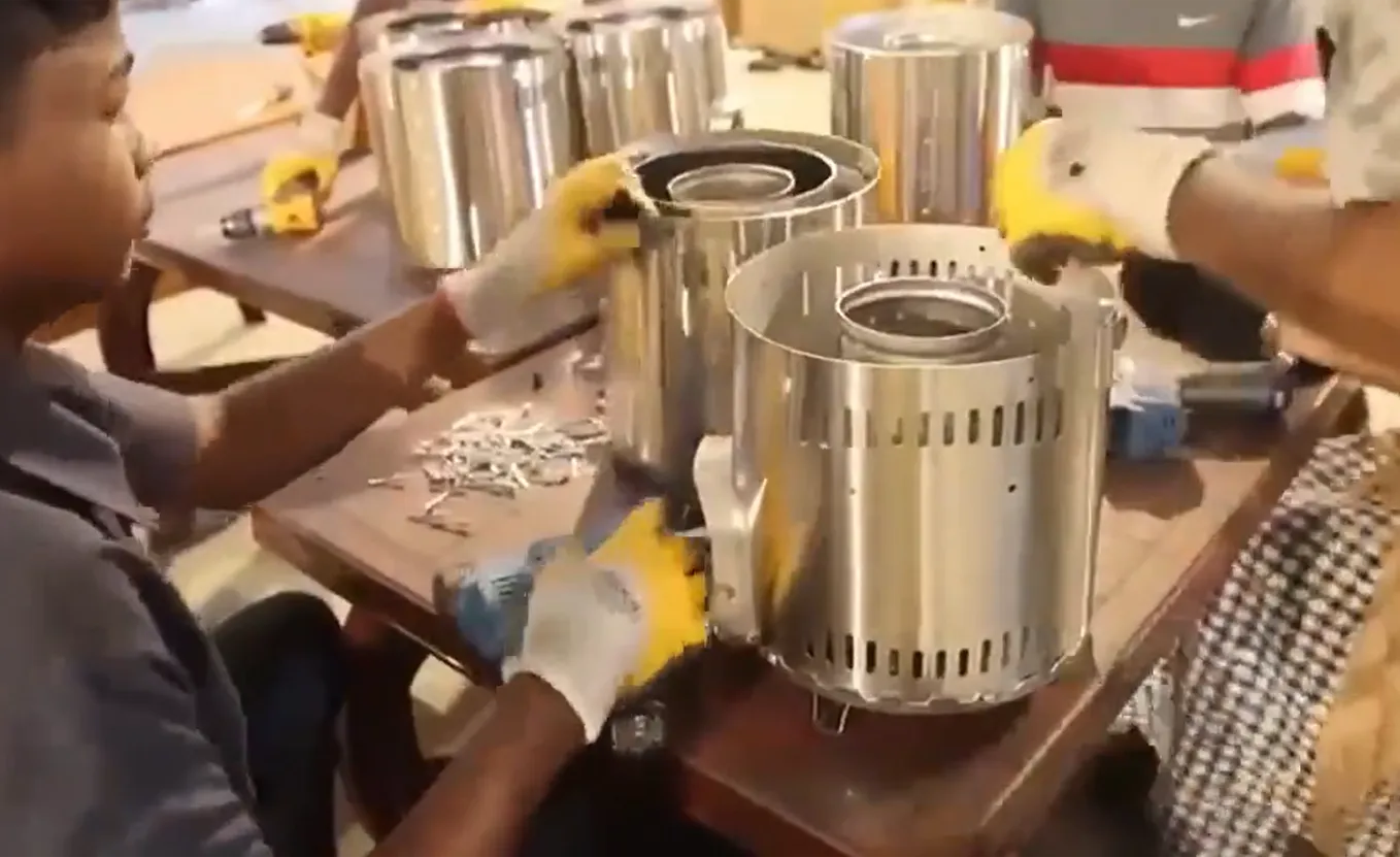 Local assembly workers wearing protective gloves and working together around a table to assemble stainless steel biomass cookstoves at SSM's local assembly project site in Sri Lanka.