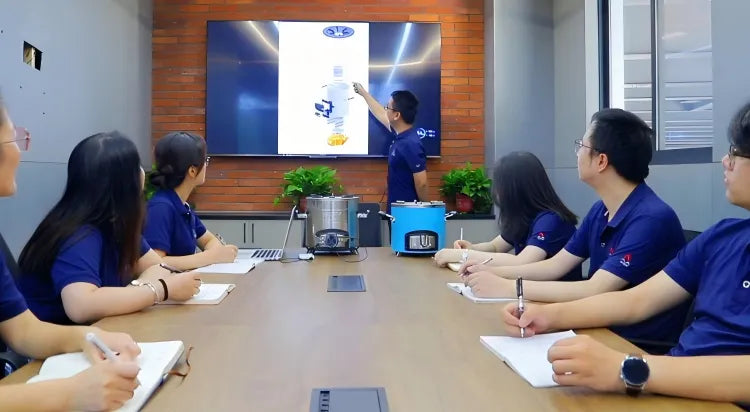 A professional team in matching blue uniforms during a design and testing meeting at Zhejiang Huiwenmei Stove Co., Ltd. (SSM), with a presenter explaining stove schematics on a large display screen and biomass stove prototypes placed on the conference table.